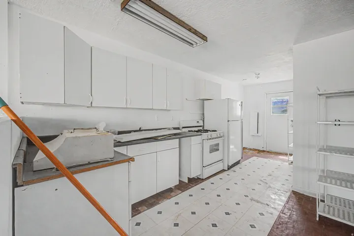 Kitchen featuring white cabinetry, a freestanding gas range, a refrigerator, a utility sink, and mixed flooring surfaces