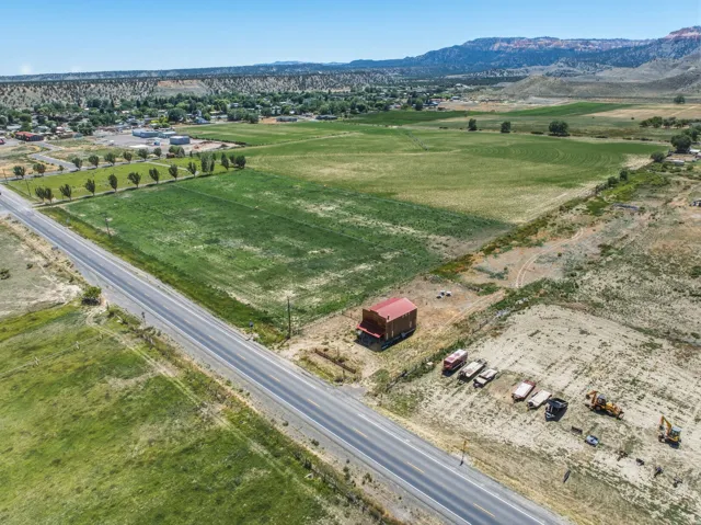 Expansive agricultural land featuring a paved road frontage, a red barn structure, and distant mountain backdrops