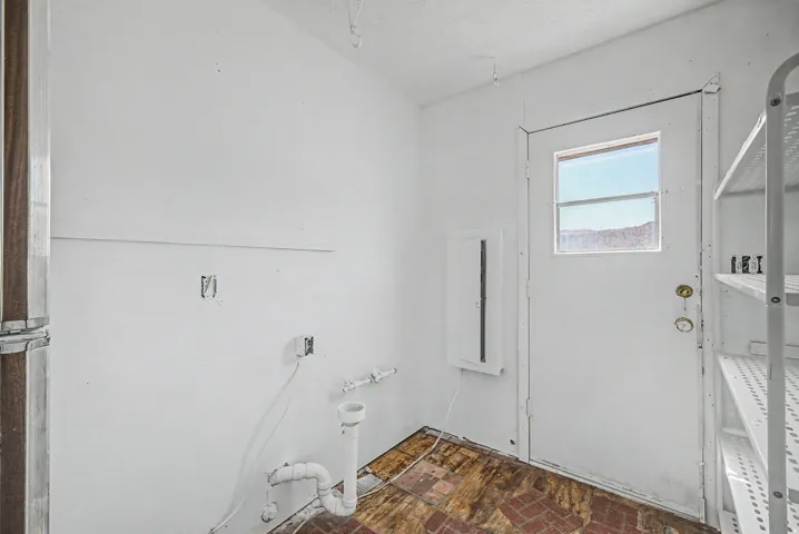 Service area featuring a rear door with a window, exposed plumbing, a circuit breaker panel, and an adjacent built-in shelving unit