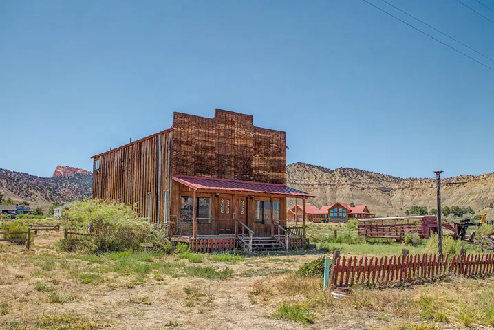 Rustic wood-sided building featuring a red metal roof and a covered front porch with a railing