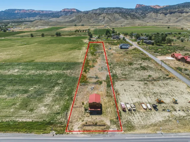 Expansive parcel featuring a red-roofed structure, roadside frontage, and surrounding open land