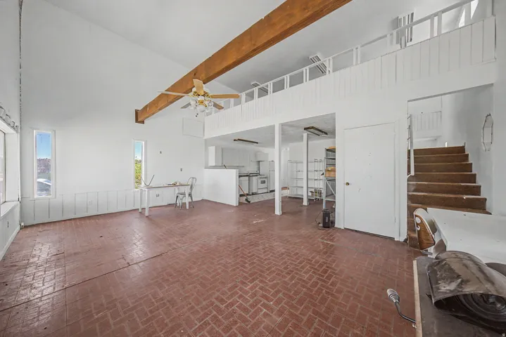 Expansive great room featuring a vaulted ceiling with exposed wood beams, herringbone brick-finish flooring, and multiple windows