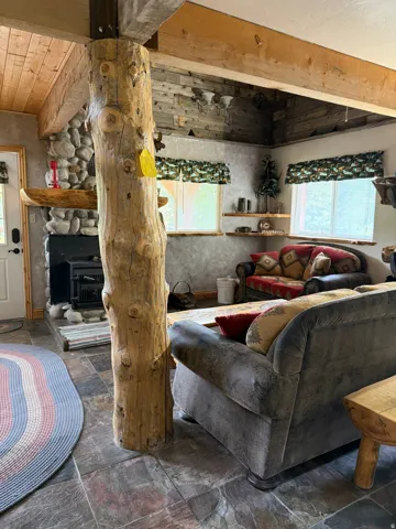 Living area featuring a prominent natural wood structural pillar, exposed wood ceiling beams, and stone-clad fireplace with an insert