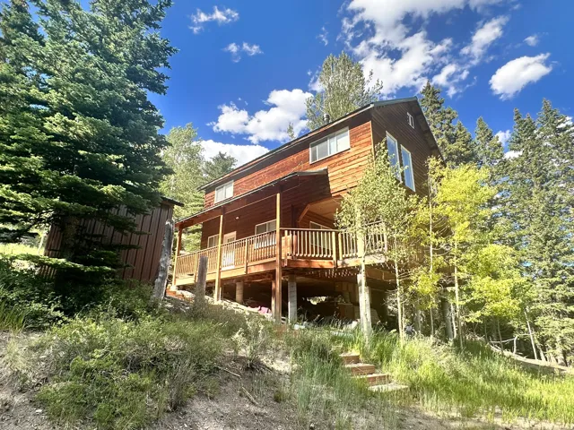 Wood-sided mountain home featuring multiple windows, an elevated deck with wood railings, and a secondary wood structure