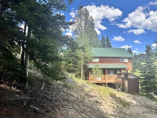 Wood-sided cabin featuring a green metal roof, a full-length covered porch, and an elevated wood deck