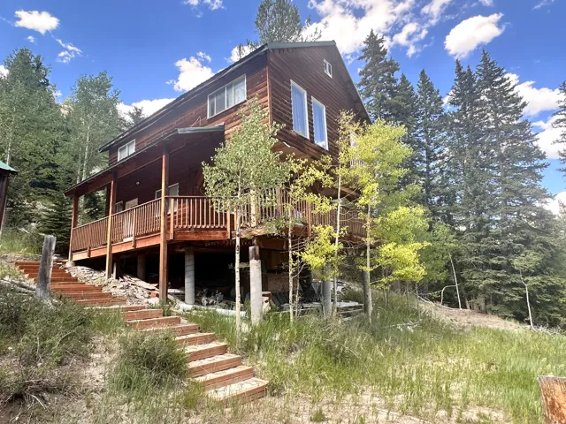 Two-story wood-sided property featuring a covered porch, an upper-level balcony with railings, multiple large windows, and a multi-tiered outdoor staircase
