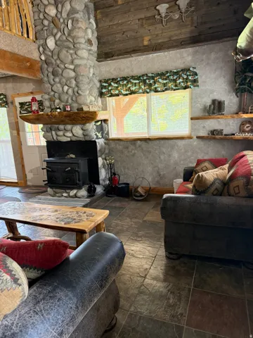 Living area featuring a floor-to-ceiling river rock fireplace with a wood-burning stove, a natural wood mantel, and slate tile flooring