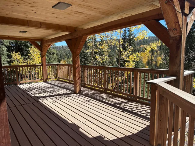 Spacious covered deck featuring wood-finish flooring, robust timber framing, and a wooden railing system