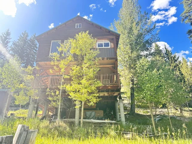 Multi-level cabin-style home featuring a wood-siding exterior, an upper-level balcony with wood railings, and an expansive sloped lot with mature trees