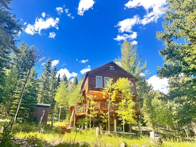 Log cabin with multiple levels and a wrap-around deck surrounded by mature trees