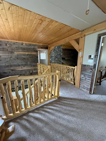 Rustic wood railing and paneling on upper level, featuring wood-plank ceiling and stone-clad architectural elements
