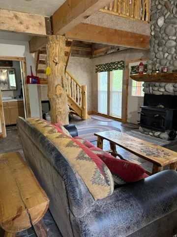 Rustic interior with a prominent log column, exposed wood beams, a stone fireplace with a wood-burning stove, a log staircase, and wood-finish flooring