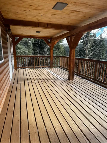 Expansive covered deck featuring natural wood flooring and railing, exposed wood beam construction, and a planked wood ceiling with recessed lighting