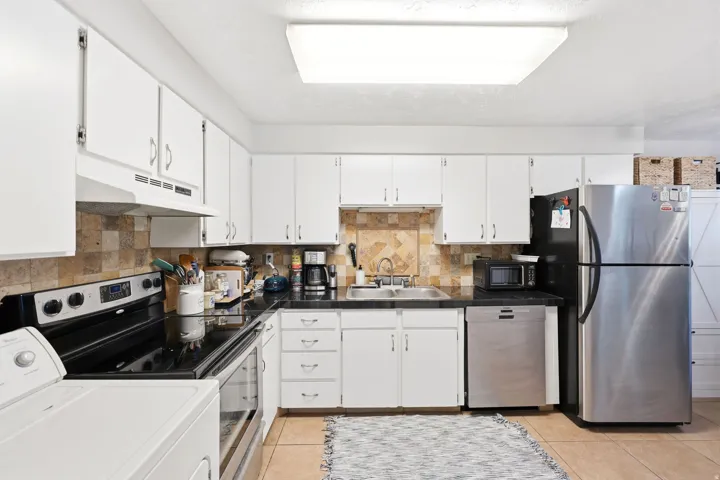 Kitchen featuring white cabinetry, black countertops, stainless steel refrigerator, stainless steel dishwasher, and tiled backsplash