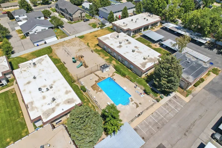 Outdoor swimming pool with concrete surround, fenced playground area, multiple residential buildings, and dedicated parking spaces