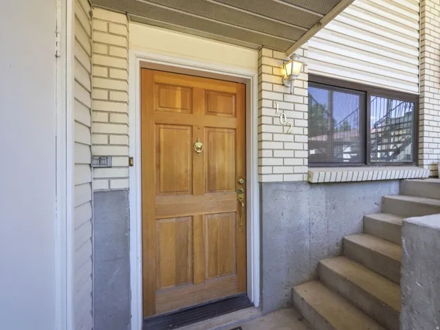 Front entry featuring a paneled wood door with knocker, concrete foundation, light-colored brick facade, and concrete steps