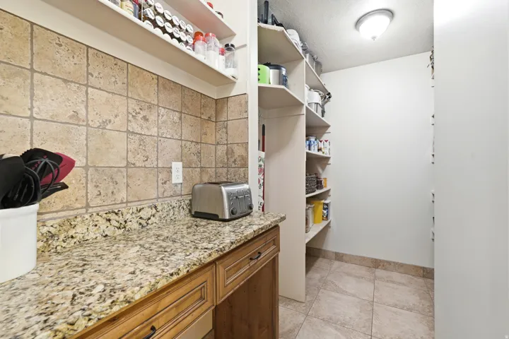 Kitchen pantry with granite-finish countertop, tiled backsplash, and wood-finish cabinetry