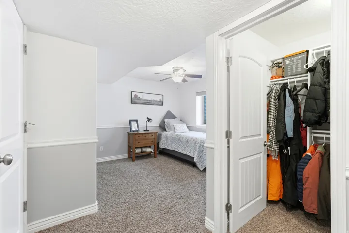 Carpeted room featuring a ceiling fan, window, and a built-in closet with shelving and hanging rods