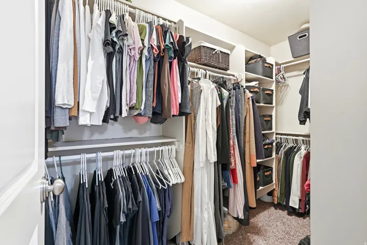 Walk-in closet featuring white built-in shelving, multiple hanging rods, and an L-shaped configuration