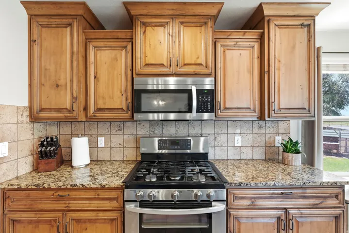 Kitchen featuring wood cabinetry, stainless steel range with gas cooktop, stainless steel microwave, stone tile backsplash, and speckled countertops