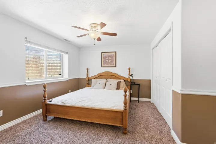 Carpeted room featuring a ceiling fan with integrated lighting, a window with blinds, bi-fold closet doors, and two-tone painted walls with chair rail molding