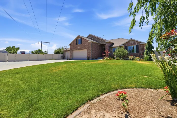 Brick exterior residence featuring a two-car garage, mature landscaping, a paved driveway, and a fenced perimeter