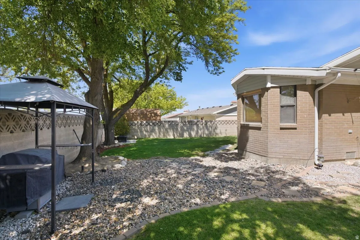 Spacious rear yard featuring an established tree, gravel accents, and a manicured lawn