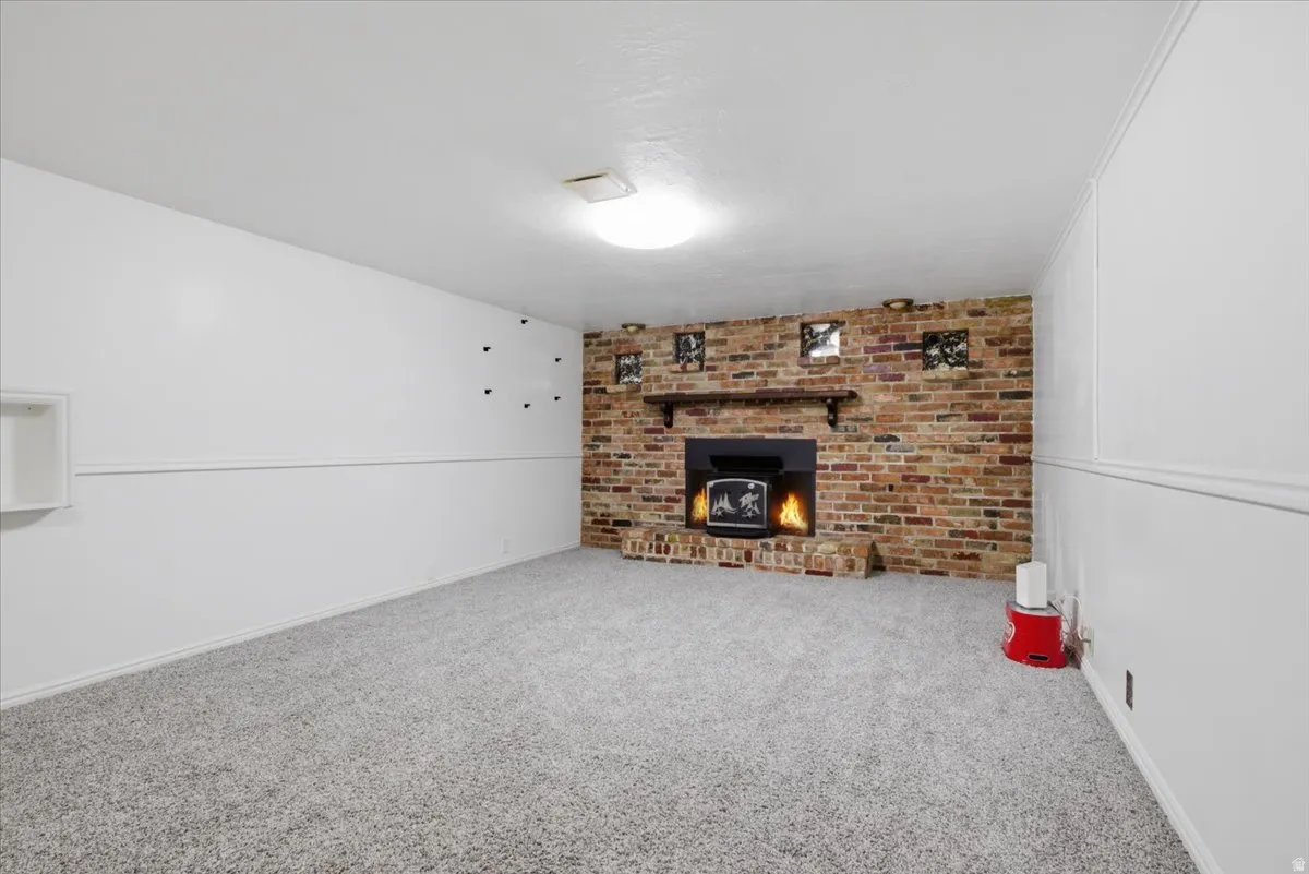 Spacious room featuring a brick fireplace with a dark mantel, light gray carpet, and white walls with a chair rail