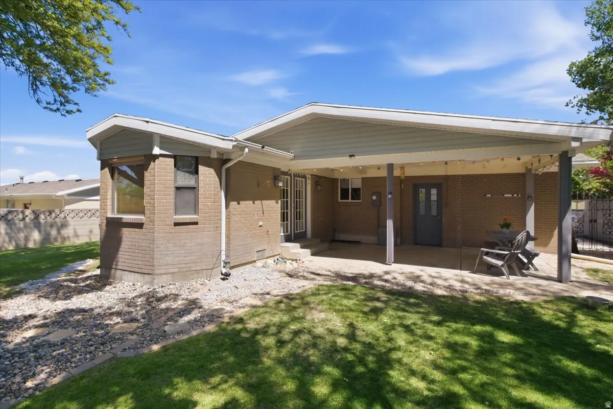 Expansive brick exterior featuring a covered patio with string lights, dual French doors, a bay window, and a gravel perimeter with stepping stones