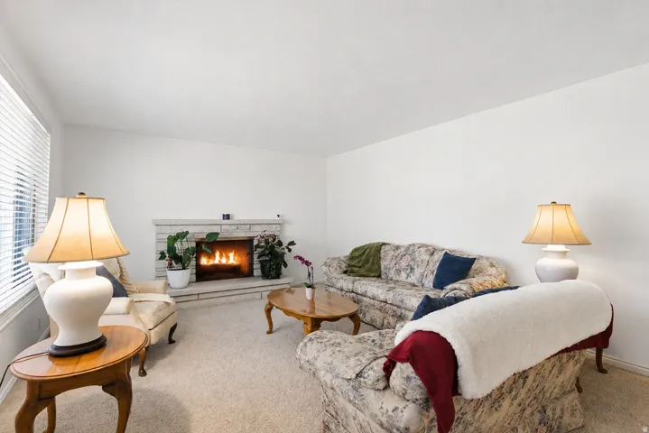 Living area featuring a stone-clad fireplace, light-toned carpeting, and white walls