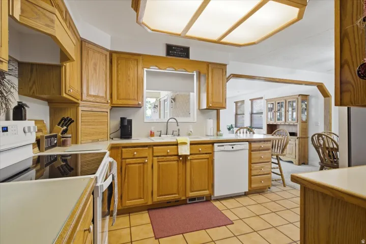 Kitchen featuring wood cabinetry, white appliances, light countertops, and tile flooring