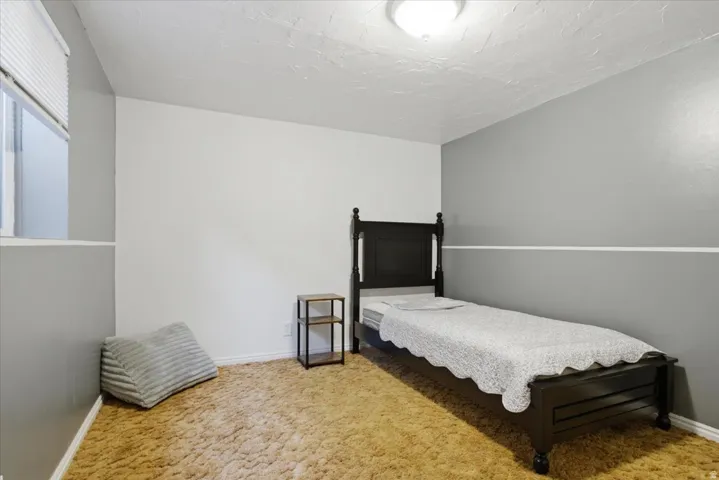 Interior room featuring a window with white blinds, textured white ceiling, and two-tone wall paint in gray and white