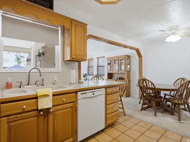 Kitchen area featuring wood cabinetry, a double basin sink with a window, white countertop, and integrated dishwasher