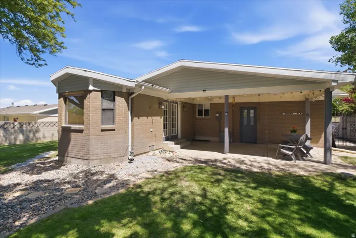 Expansive brick exterior featuring a covered patio with string lights, dual French doors, a bay window, and a gravel perimeter with stepping stones