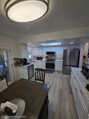 Modern kitchen featuring white cabinetry, stainless steel appliances, a tile backsplash, light wood-finish flooring, and a skylight