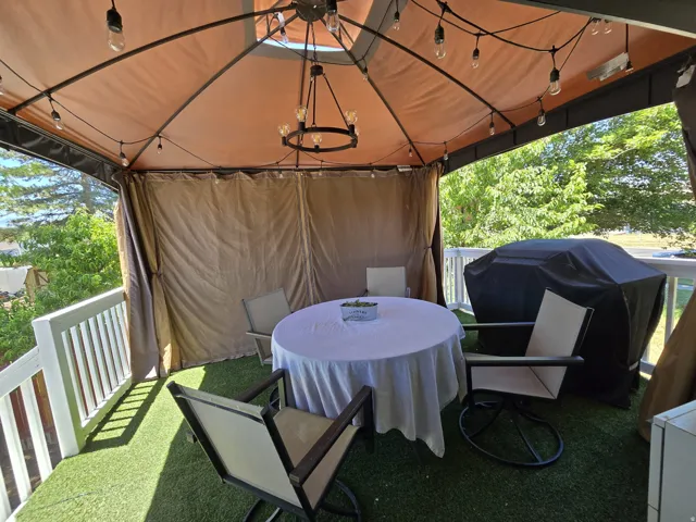 Covered outdoor deck with string lighting, a central chandelier, privacy drapes, and artificial turf flooring
