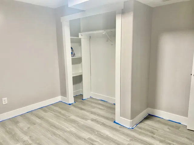 Built-in closet featuring white shelving and a hanging rod, complemented by light gray wood-finish flooring and white baseboards