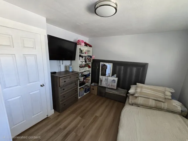 Interior room featuring wood-finish flooring, light gray walls, a white paneled door with a silver knob, and a flush-mount ceiling light with a brushed nickel finish