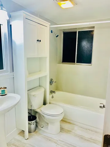 Bathroom featuring a built-in tub with shower, white pedestal sink, and a tall storage cabinet with open shelving