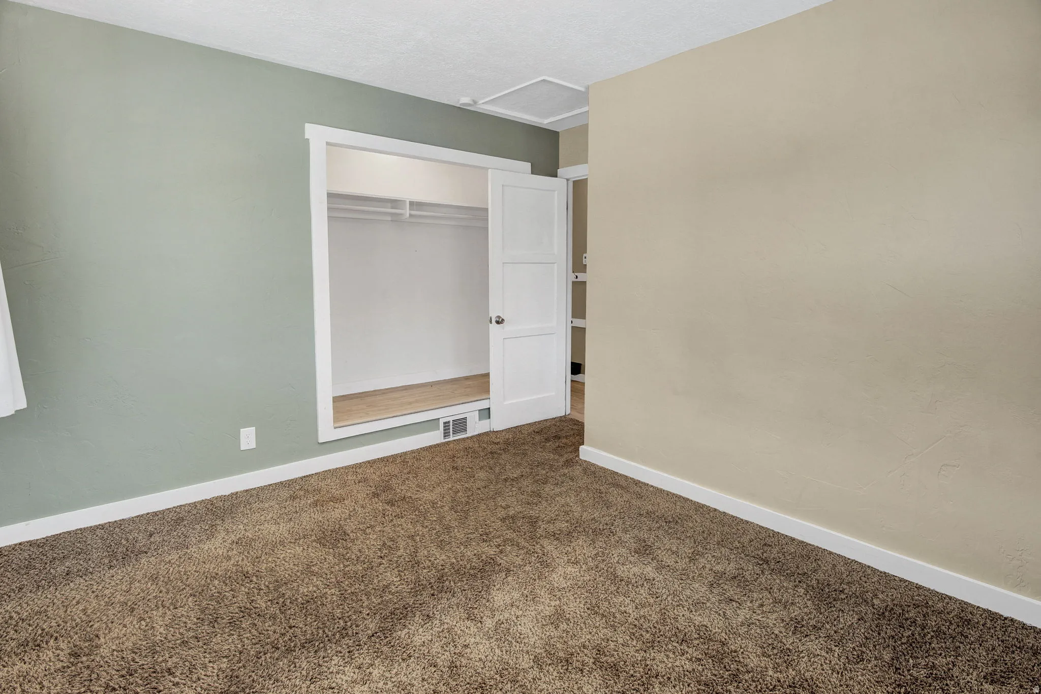 Carpeted room featuring a built-in closet with wood-finish flooring and bi-fold doors, complemented by white baseboards