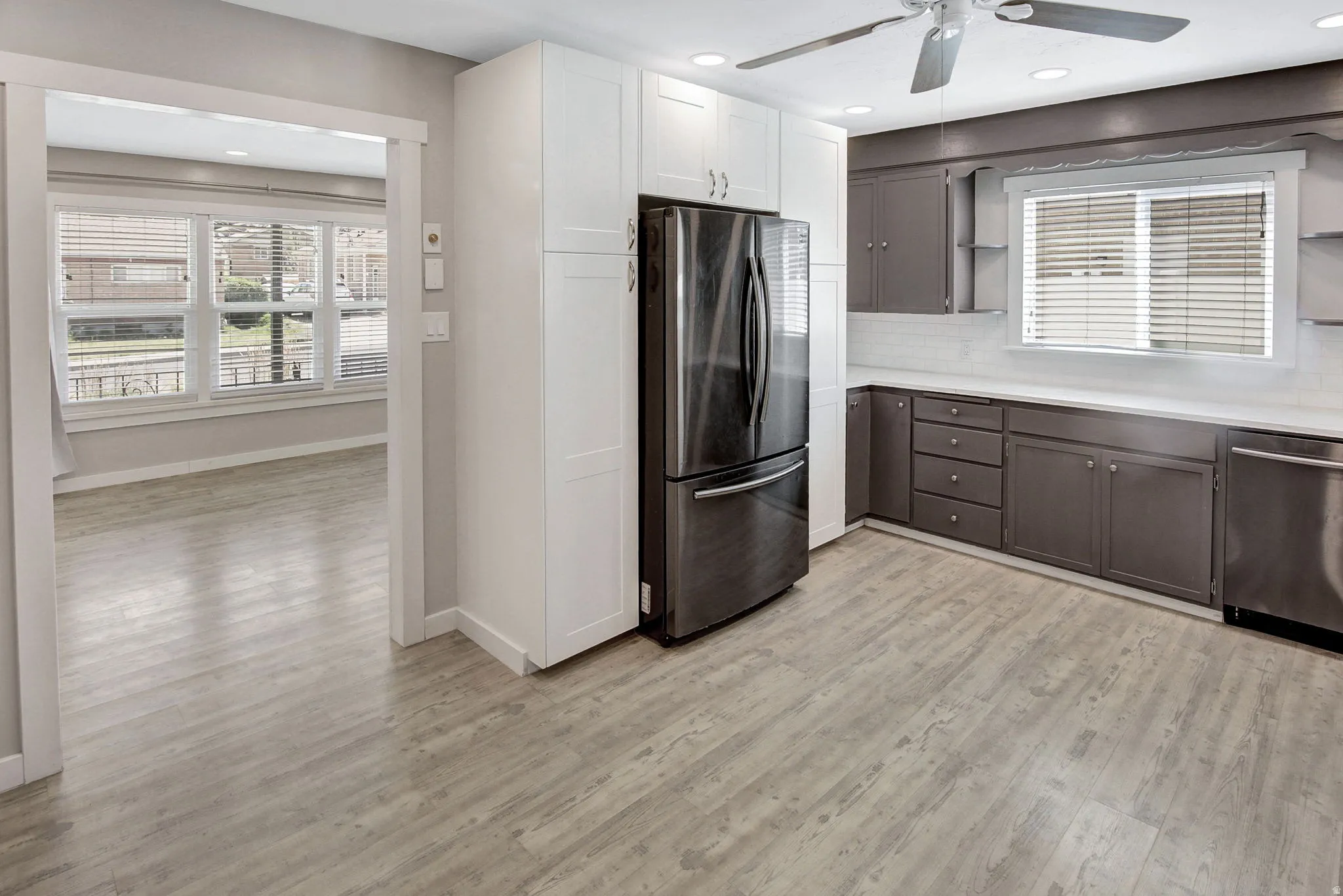 Modern kitchen featuring wood-finish flooring, two-tone cabinetry with white upper and dark lower units, stainless steel appliances, and a white countertop