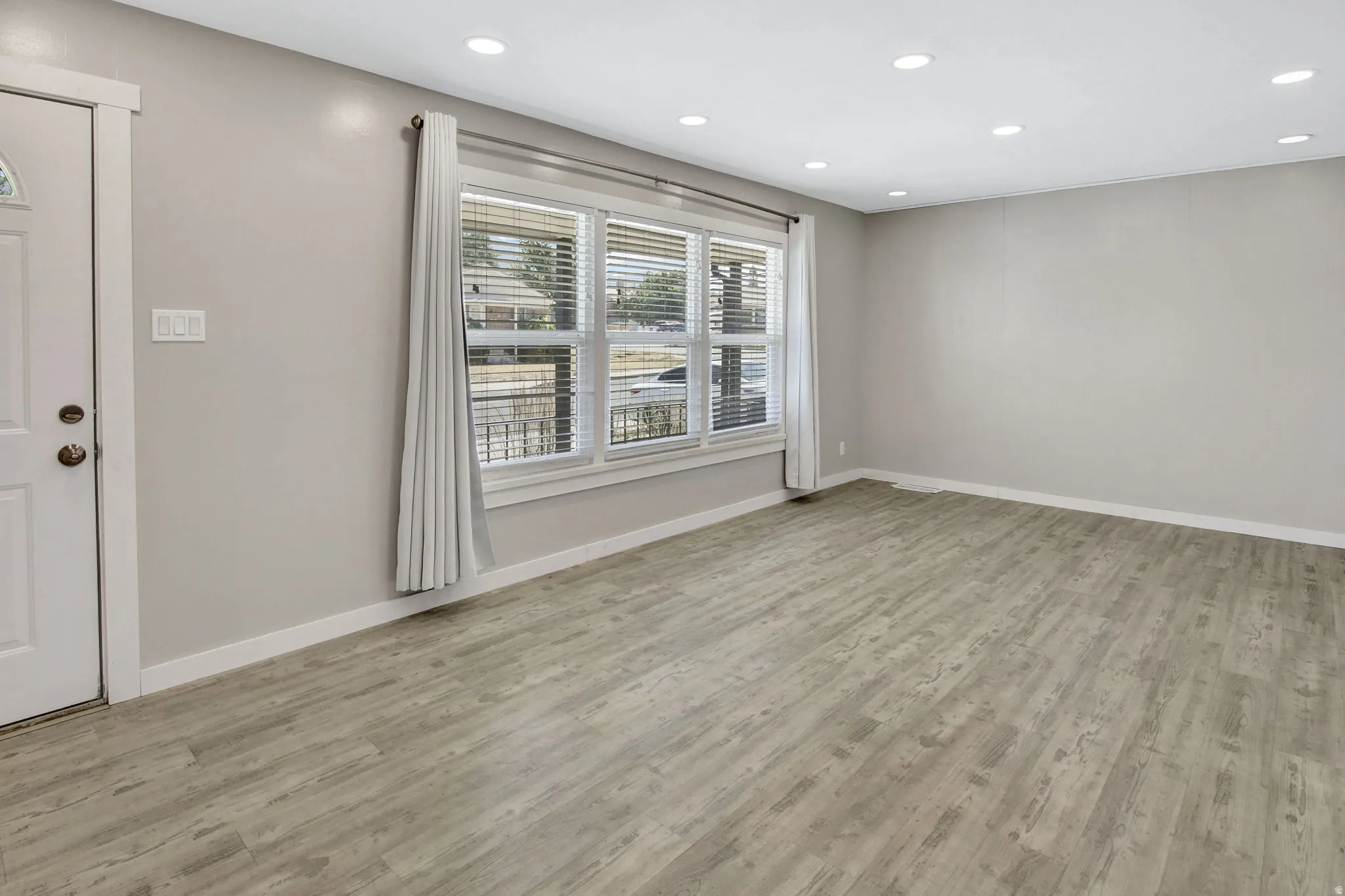 Spacious room featuring wood-finish flooring, recessed lighting, and a large window with blinds