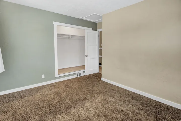 Carpeted room featuring a built-in closet with wood-finish flooring and bi-fold doors, complemented by white baseboards