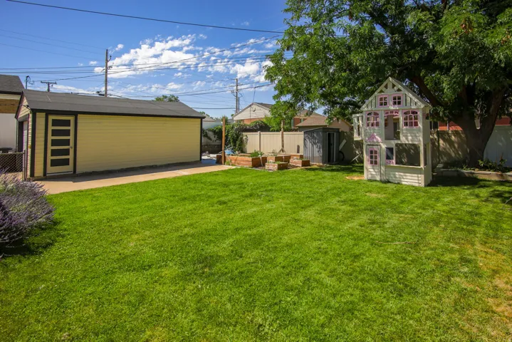 Expansive grassy yard with a detached garage featuring a contemporary side entry door, mature perimeter trees, and a concrete pathway