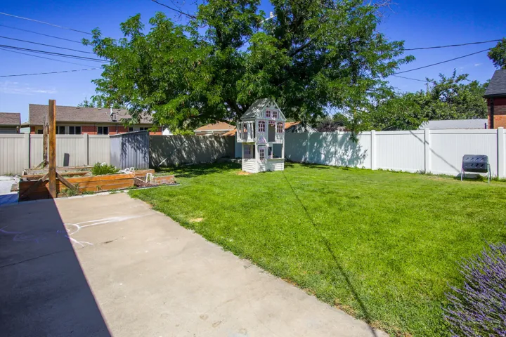 Expansive backyard featuring a large grass lawn, mature tree, raised garden beds, and substantial fencing