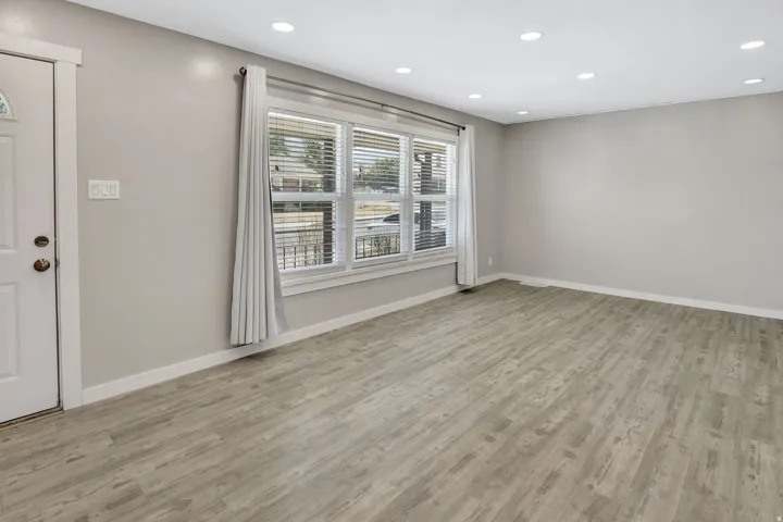 Spacious room featuring wood-finish flooring, recessed lighting, and a large window with blinds