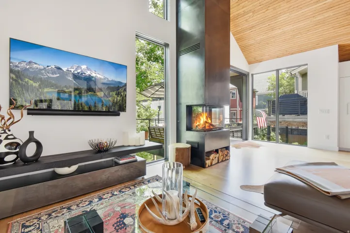 Vaulted wood-finish ceiling covering a living area featuring a built-in media console, wood-finish flooring, full-height windows, and a modern fireplace with integrated wood storage