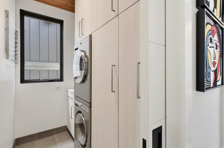 Laundry area featuring stacked appliances, ample built-in cabinetry with modern hardware, and a wood-finish ceiling