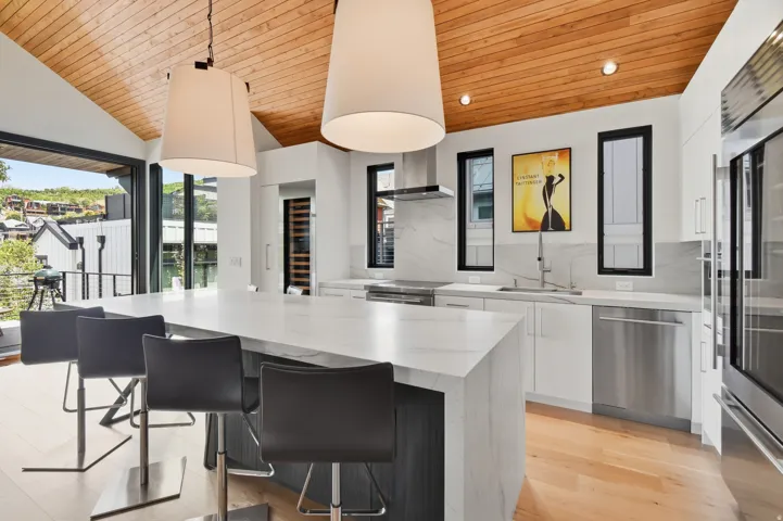 Gourmet kitchen featuring a large waterfall island with seating, stainless steel appliances, a built-in wine cooler, and expansive floor-to-ceiling sliding glass doors