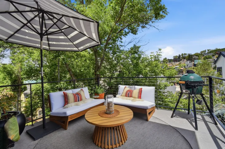 Expansive outdoor deck featuring cable railing, a built-in barbecue, and mature tree surroundings